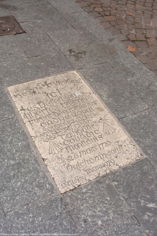 Le granit résiste 30 ans après la pose et est encore très lisible. Pierre de granit clair poli scellée dans le sol en granit gris foncé (qui a été refait – depuis la pose de la plaque en la respectant – quand le quartier est devenu piétonnier). Croix du s