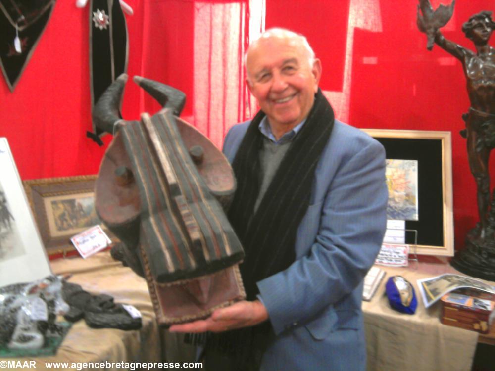 Jean Laick avec une sculpture d'art africain représentant d'un côté une tête de crocodile et de l'autre des cornes de buffles