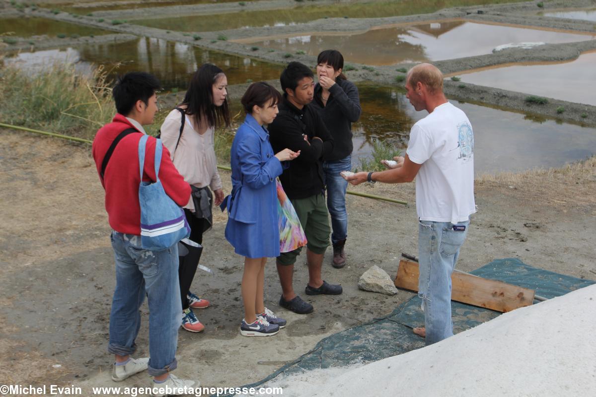 Le paludier Frédéric Lelant présente à l'équipe de tournage le sel gris et la fleur de sel.  Maya Kobayashi porte un manteau bleu.