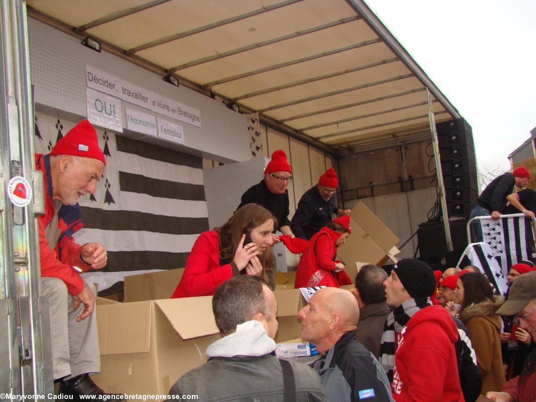 14 h 26. En attendant les discours, vente de bonnets rouges d’abord sur le podium.