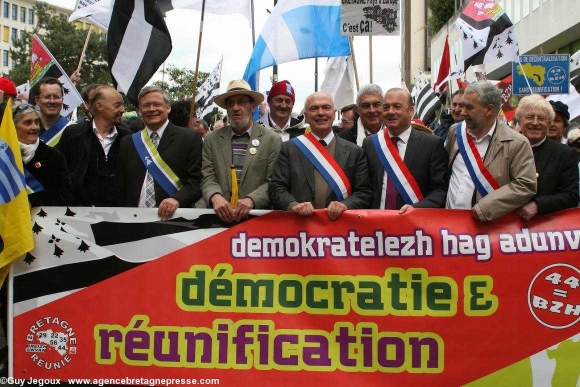 Derrière la grande banderole <i>Démocratie et réunification</i> bilingue : Mona Bras, Christian Guyonvarc'h, Alan Stivell, Gérard Lahellec, Herri Gourmelen, Marc Le Fur, Thierry Benoît, Ronan Dantec, Yvon Mahé. Manifestation historique de Nantes le 19 avril 2014 pour la réunification de la Bretagne.